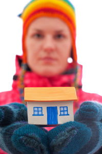 Person in hat and mittens holding a model house
