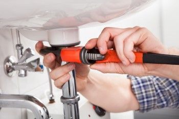Plumber tightening a pipe underneath a sink