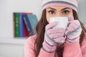 Woman wearing a hat and gloves and holding a mug while indoors